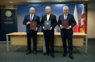 Na zdjęciu cztery osoby stoją w szeregu podczas oficjalnej uroczystości, każda trzyma teczkę z herbem Województwa Lubelskiego i napisem