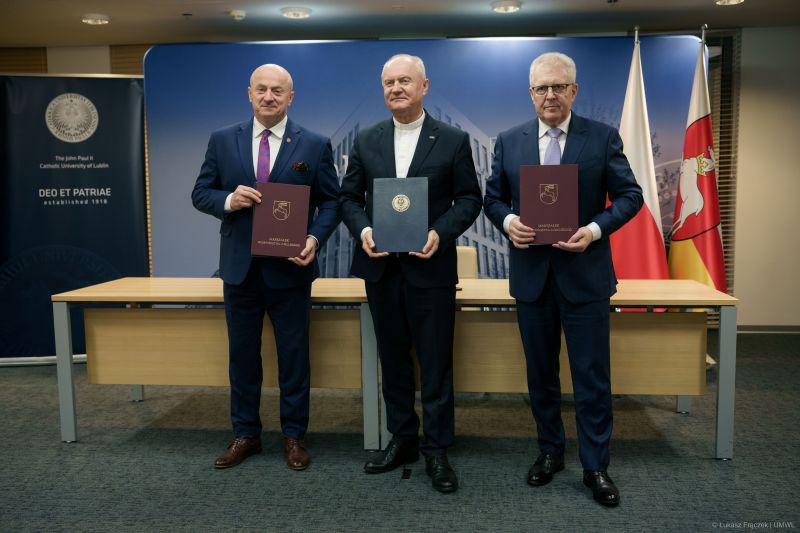 Na zdjęciu cztery osoby stoją w szeregu podczas oficjalnej uroczystości, każda trzyma teczkę z herbem Województwa Lubelskiego i napisem "Marszałek Województwa Lubelskiego". Od lewej: Jarosław Stawiarski, Marszałek Województwa Lubelskiego, ks. prof. Mirosław Kalinowski rektor Katolickiego Uniwersytetu Lubelskiego, Piotr Matej, dyrektor Wojewódzkiego Szpitala Specjalistycznego im. Stefana Kardynała Wyszyńskiego w Lublinie; Zdjęcie wykonano w sali konferencyjnej podczas podpisania porozumienia o współpracy.