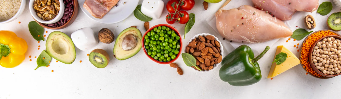 Kolorowy baner przedstawiający zdrową żywność: warzywa, owoce, orzechy, rośliny strączkowe oraz kawałki ryby i drobiu rozmieszczone na jasnym tle, symbolizujące zbilansowaną dietę i żywienie dla zdrowia.