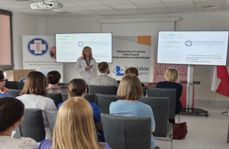 Obraz przedstawia Panią dr Małgorzata Piasecka, dyrektor ds. Lecznictwa w trakcie prelekcji w ramach warsztatów.