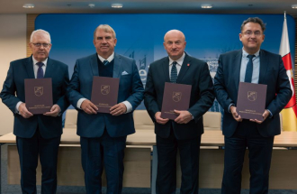 Na zdjęciu cztery osoby stoją w szeregu podczas oficjalnej uroczystości, każda trzyma teczkę z herbem Województwa Lubelskiego i napisem 